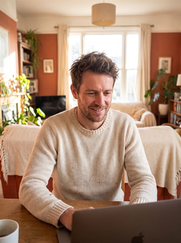 An adult working calmly at a laptop in a bright, homely room.